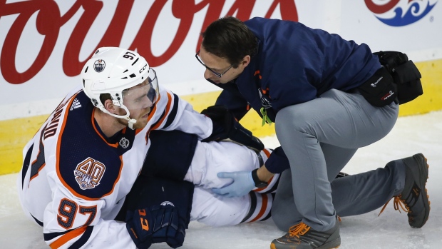 Connor McDavid, left, has his knee tended too after crashing into Calgary Flames goalie Mike Smith