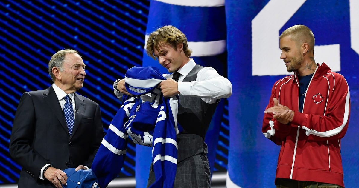 Photo: tsn.ca Gavin McKenna, centre, puts on a jersey after being drafted by the Toronto Maple Leafs as NHL Commissioner Gary Bettman
